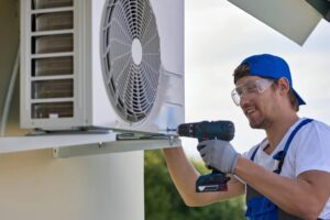 Caucasian worker installs outer metal case air conditioner with screwdriver AC Installation Service Near You MetroHandz